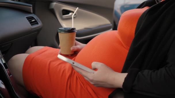 Nierozpoznawalna Ciężarna Kobieta Pomarańczowej Sukience Samochodzie Pijąca Kawę Korzystająca Internetu — Wideo stockowe