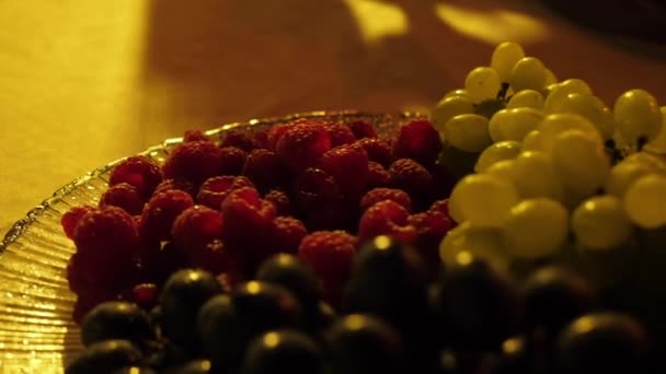夕暮れ時に皿の上にラズベリー 緑と黒のブドウを熟すクローズアップ — ストック動画