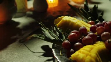 Meyveler, titreyen mum ışığıyla aydınlatılmış masanın üzerinde.