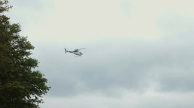 Helikopter gökyüzünde yavaşça uçuyor ve bulutlu bir günde elektrik hatlarını inceliyor.