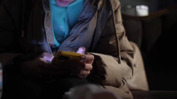 一个无法辨认的女人晚上在一个城市街道咖啡馆里使用智能手机 女性的手在手机上输入信息 — 图库视频影像