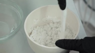 Bir kozmetolojistin elleri kremin içine beyaz toz karıştırır. Bir yüz maskesi hazırlayan güzellik uzmanı yüz bakımını hazırlıyor. Kozmetoloji. Cilt için aljinat maskesi hazırlayın.