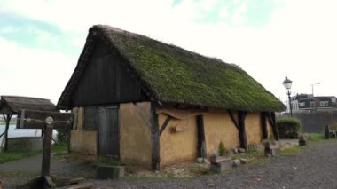 Bulutlu bir günde nehir kıyısında sazdan çatısı olan eski bir taverna. Duvardaki tabelada Taveerne yazılıydı.
