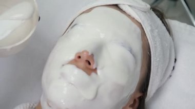 Kozmetik ve kaplıca, beyaz maske bir güzellik salonundaki hastaların yüzünü ve gözlerini kapatır. Tanımlanamayan kadın yüz bakımı görüyor.