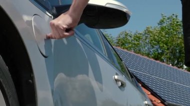 Fotovoltaik şarj istasyonunda elektrikli bir otomobilin fişini takan tanınmayan bir adam. Erkek eller, güneş panelleri arka planında EV, elektrikli araba veya PHEV şarj etmek için güç kablosu tedariki bağlar