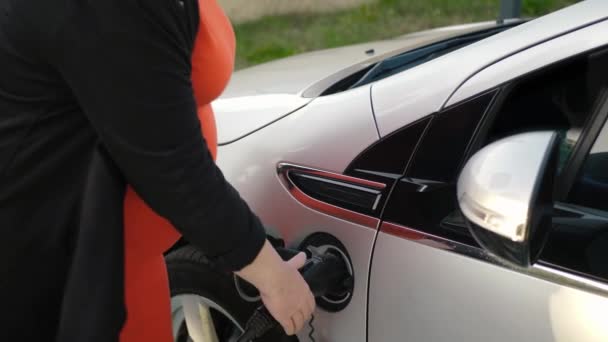 女性の手はEv車かPhevに電源コネクターを挿入します 電気自動車に充電ケーブルを差し込んで電池を充電するドレスの認識できない妊婦 Evプラグを接続する — ストック動画