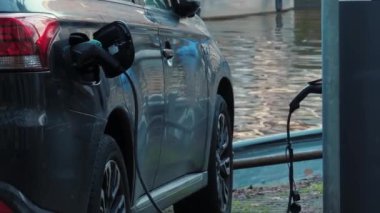 Otoparkta yenilenebilir enerji kaynaklarıyla EV şarj ediliyor. Bir elektrikli araç su kanalının yakınındaki şarj istasyonunda şarj oluyor. Elektrikli araba aküsü şarjı.