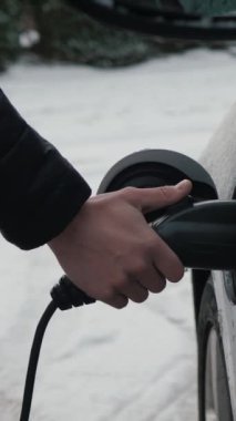 Erkek ellerinin dikey videosu EV 'den güç bağlantısını kesiyor, kar kapanıyor. Tanımlanamayan kişi elektrik kablosunu elektrikli arabadan ayırıyor. Kışın pilleri elektrikli araç veya PHEV şarj etmek