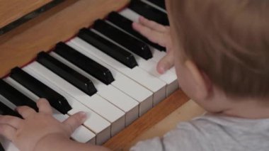 Bebek piyano çalmaya çalışıyor, müzik öğreniyor. Çocuk müzisyenlerin elleri piyano çalmayı öğreniyor, müzik aleti, yakın plan. Küçük çocuk parmakları piyano tuşlarına basar