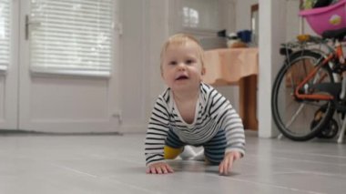 Enerjik küçük bir çocuk, çizgili kıyafetler giymiş, sıcak fayans zemininde sürünüyor. Komik bebek ilk kez etrafındaki dünyayı anlamaya çalışıyor.