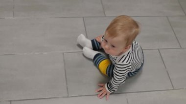 Sevimli, uykulu ve düşünceli bir erkek bebeğin portresi çizgili giysiler içinde sıcak fayans zemininde oturuyor, üst manzara. Rüya gören küçük çocuk, boşluğu kopyala