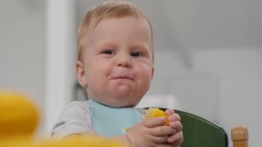 Sevimli küçük bebek elinde parlak bir mısır parçası tutuyor ve meraklı bir şekilde kameraya bakıyor, gülümseyen bebek. Bu video yemek ve çocukla ilgili konular için ideal, neşe ve masumiyet yayıyor.