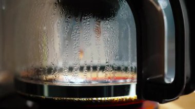 Bir kahve makinesinin yakın çekimi bardakta buhar yoğunlaştığını ve damlaların düştüğünü gösteriyor. Günlük rutinlerimizdeki kahve önemini ve kahvaltıdaki rahatlatıcı varlığını vurguluyor.