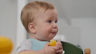 Bebek bebek yüksek bir sandalyede oturur, şevkle tatlı mısırı yer, parlak bir ortamda saf mutluluk ve merak yayar.