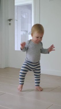 Mutlu bebek aydınlık odada ilk adımlarını atıyor. Bebek yürüyor, fayanslı zemine basıyor, ayaklarıyla ilk mutlu adımlarını atıyor. Bebek çocuk saf heyecan ve şevkle, eğlenceye hazır.