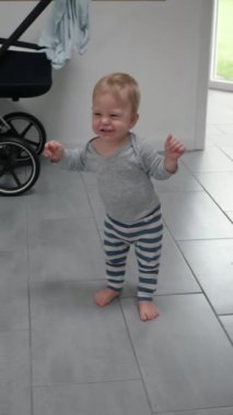 Mutlu bebek ilk adımlarını atıyor, kameraya bakıyor. Bebek yürüyor, fayanslı zemine basıyor, ayaklarıyla ilk mutlu adımlarını atıyor. Bebek çocuk saf heyecan ve şevkle, eğlenceye hazır.