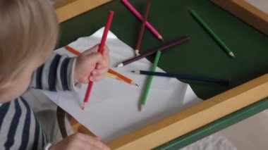 Çocuk ahşap bir masadaki kağıt bir yaprak üzerinde parlak kalemlerle boyuyor. Bebekler sanatsal ifade ve oyun sahnesinde yaratıcılığı keşfediyorlar.