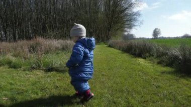 Açık mavi giysili küçük bir çocuk elinde sopa tutuyor. Küçük çocuk, uzun ağaçlarla çevrili güneşli, parlak yeşil araziyi keşfeder. Doğanın sükunetini gerçekten canlandırır..