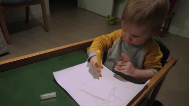 Çocuk, ahşap yeşil masada kağıt üzerine sarı kalemle boyuyor. Ufaklık sanatsal ifadenin keyifli sahnesinde yaratıcılığı keşfediyor
