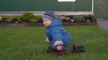 Parlak mavi bir ceket giymiş neşeli bir çocuk paslı bir oyuncak trende mutlu bir şekilde oturur, yemyeşil bir çimenlikte oynar, huzurlu açık hava ortamının tadını çıkarır.