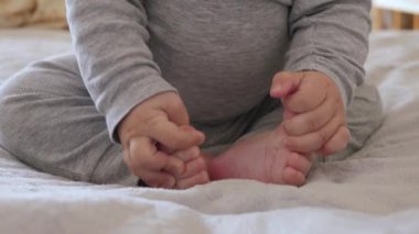 Tanımlanamayan bebek, rahat bir battaniyenin üzerinde ayaklarına ve ayak parmaklarına dokunarak oturuyor. Bebekler küçük eller ve ayaklar masumiyet ve rahatlık duygusunu barışçıl bir şekilde tamamen somutlaştırır.