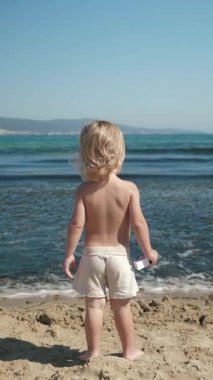 Güzel, sıcak bir günde dikey bir video, tasasız bir çocuk kıyıları keşfeder, nazik dalgaların yanında durur, doğanın çarpıcı güzelliği arasında çocukluğun saf masumiyetini yakalar.