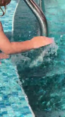 Havuz kenarında oynayan mutlu çocukların ellerini gösteren dikey bir video. Serinletici suyun ve güneşin tadını çıkarıyorlar. İnanılmaz bir tatil sırasında, yavaş çekim, yakın çekim.