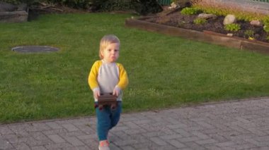 Küçük çocuk dışarıda oynarken paslı, ağır bir oyuncak araba taşıyor. Çocukluğun masumiyetini ve mutluluğunu temsil ediyor.