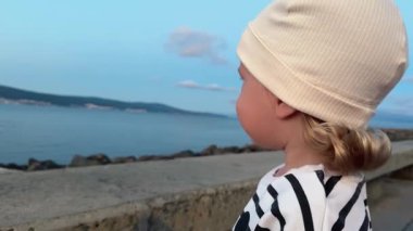 Gün batımında okyanus kıyısında huzur içinde duran küçük çocuk büyüleyici bir günbatımında doğanın çarpıcı güzelliğine dalmış masumiyet ve merakı somutlaştırıyor.