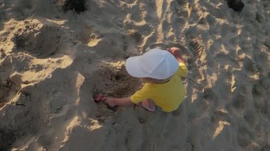 Bebeğim, parlak sarı tişört ve şirin beyaz şapka giyip kumsaldaki yumuşak kumda neşeyle oynuyor. Yürümeye başlayan yaratıcı aktiviteler, güneşli bir geceye kucak açan ve eğlenceli, üst görünüm
