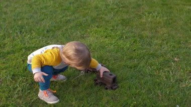 Yürüyen çocuk dışarıda oyun oynarken yeşil çimenlerin üzerinde paslı bir oyuncak treniyle mutlu bir şekilde oynuyor, çocukluğun masumiyetini ve mutluluğunu somutlaştırıyor.