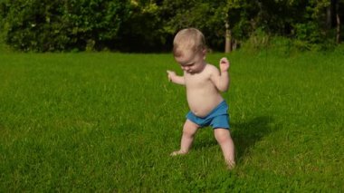 Neşeli mutlu çocuk yeşil çimlerle çevrili bir çimenlikte duruyor, parlak mavi şort giyiyor, çocukluk ve özgürlüğün keyfini çıkarıyor..