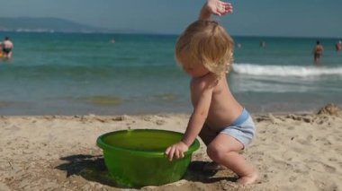 Neşeli küçük çocuk deniz kenarında mutlu bir şekilde oynuyor. Parlak yeşil bir küvetten sıcak kumlu sahile su sıçratıyordu. Yaz eğlencesinin ve neşesinin gerçek ruhunu yakalıyordu.