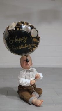 Canlı ve şenlikli bir atmosferde, şirin küçük bir bebek hayatının en güzel zamanını renkli bir doğum günü balonuyla oynayarak geçiriyor, neşe saçıyor ve saf masumiyet saçıyor.