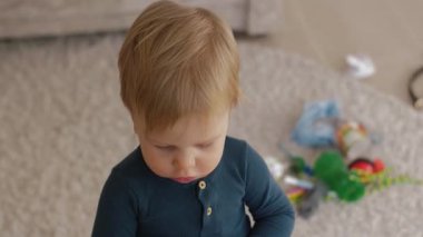 A cheerful toddler with golden-blond hair looks at the camera in a cozy living room, embodying curiosity and innocence, capturing the playful moments of everyday life