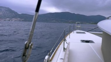Deniz kıyısının güzel manzarası ve deniz dalgalarında yüzen beyaz bir yatın tahtasından yeşil dağlar. Yat ve gemilerle deniz yolculuğu kavramı. Yat ve yelkenli turizmi.
