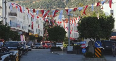 Şehir manzarası. Yeşil bir dağın zeminine karşı üç katlı bir sokak, yürüyen insanlar ve yol boyunca uzanan Türk bayraklarından oluşan bir çelenk. Kas, Türkiye - 1 Kasım 2022.