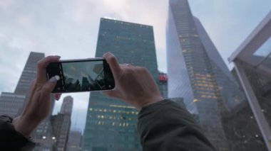 Elinde akıllı telefonu olan genç bir turistin elleri modern bir metropolün yüksek binalarını panoramik bir şekilde çekiyor. Dünya şehirlerinde turizm kavramı.