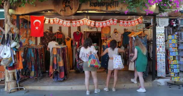 若い女性の観光客のカスグループのトルコの都市では 衣料品店の前に立つ観光客が見て それにかかってトルコの旗をストリートショップで服を選択します トルコ 2022年11月1日 — ストック動画