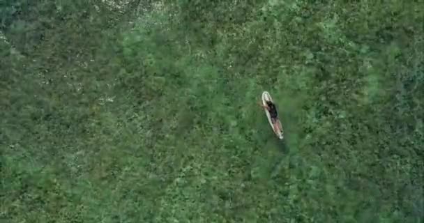 这个年轻人躺在一艘Sup船上 双手划桨 在平静的海面上漂浮着 在浅海床上的无人驾驶飞机上俯瞰全景 上面布满了汽车和一个在冲浪板上漂浮的人 — 图库视频影像