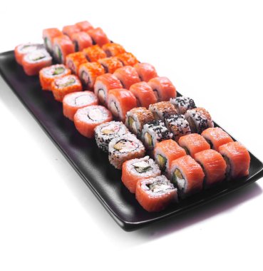 Suşi seti. Somon balıklı rulo kırmızı havyar ve siyah tabakta beyaz arka planda izole edilmiş sebzeler.