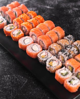 Somon, avokado, krem peynir, salatalık, pirinç, havyar, siyah masa arkasında yılan balığı.