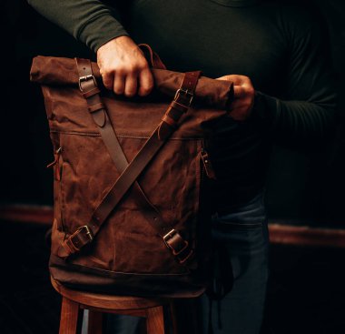 man's hand holding a canvas backpack. Model wears a brown belt bag, Medium Leather Backpack Man Rolltop Leather Rucksack Bag