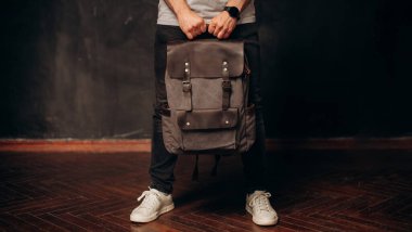 Backpack in man's hand on dark wall background. Close up canvas and leather bag