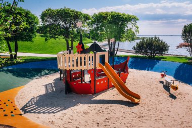 Güneşli bir günde çocukların yaratıcı oyunları için parkın yemyeşil yeşillikleri arasında yer alan ahşap bir gemi şeklinde parlak bir oyun alanı..