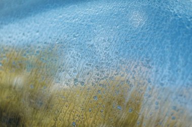 Arabanın ön camındaki su damlacıkları gün batımının parıldayan renklerini yansıtıyor. Bulanık bokeh ışıkları olan seçici bir odak. Güzel soyut doku arkaplanı.