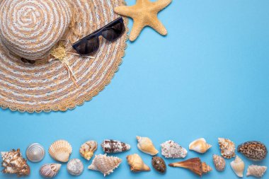 Yaz ve tatil düz yatıyordu kadın hasır şapka, güneş gözlükleri, yıldız balığı ve çeşitli deniz kabukları ile tabloların alt tarafında mavi arka planda.