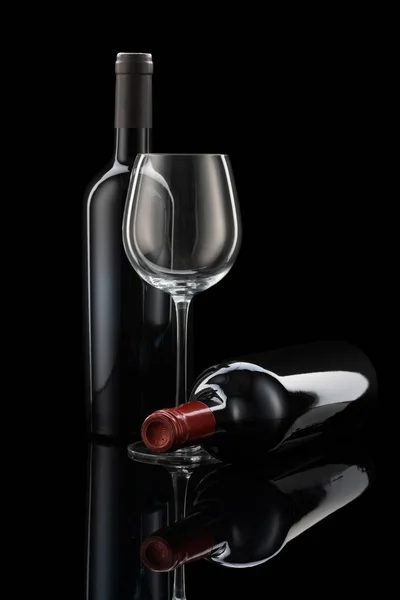 黒の背景の前に2本のワインボトル 1本のスタンドと1本の嘘とワイングラス — ストック写真