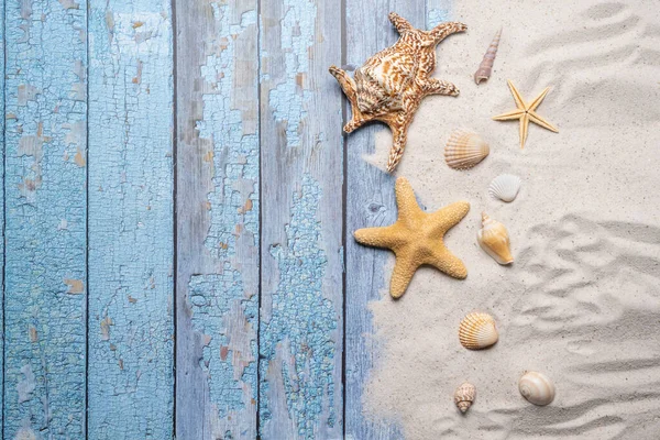 海滩和度假的概念与免费的文字空间 顶部视图 有一颗大海星和海壳的平面布局 还有各种海壳和美丽的海滩沙子 背景是蓝色的旧木板 图库照片
