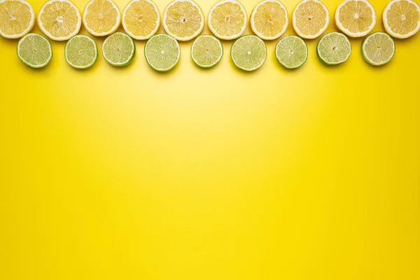 Fresh, Fruity and juicy fruit concept. View from top. Freshly cut slices of lemons and limes on the upper border of the image on a yellow background.